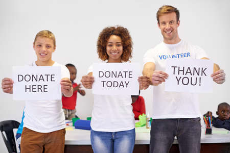 Help today. Portrait of volunteers holding up signs while working with little children.の写真素材
