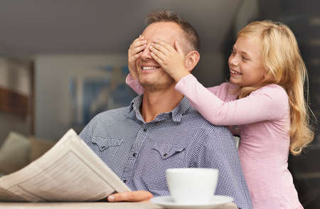 Guess who. Shot of a young girl surprising her dad by covering her hands over his eyes.の写真素材