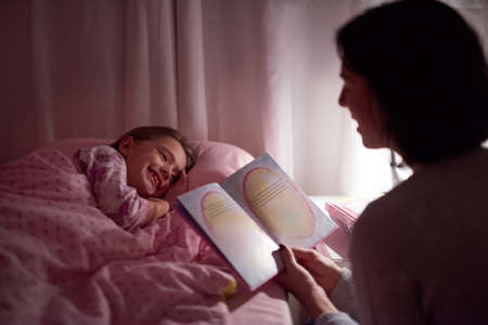 Stories to spark her sweetdreams. Cropped shot of a little girl lying in bed while her mom reads a bedtime story.の写真素材
