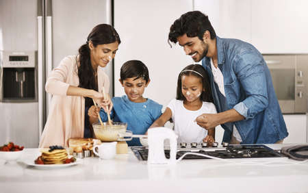 Anything you like.... Cropped shot of an affectionate young family cooking breakfast in their kitchen at home.の写真素材
