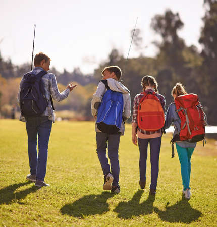 Setting off on an adventure. Shot of a group of children wearing backpacks walking together in nature.の写真素材