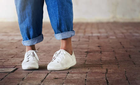 Shoes on, lets dance. Cropped shot of an unrecognizable person standing on a brick floor while wearing white sneakers and blue jeans.の写真素材