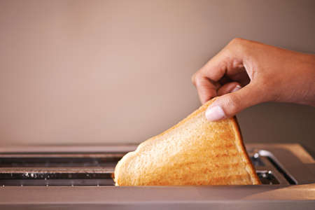 Golden brown and ready to munch. Cropped shot of a woman taking toast out of a toaster.の写真素材