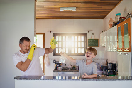 Doing chores isnt as boring as it sounds. Shot of a father and his little son having fun while doing...