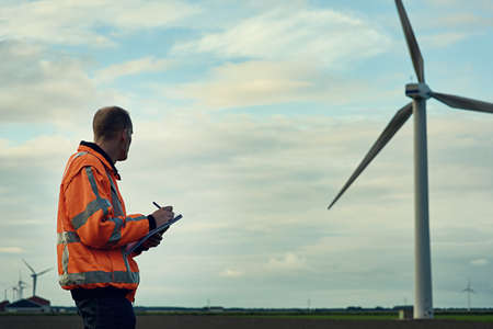 In the company of giants. Shot of a young engineer inspecting a wind turbine.の写真素材