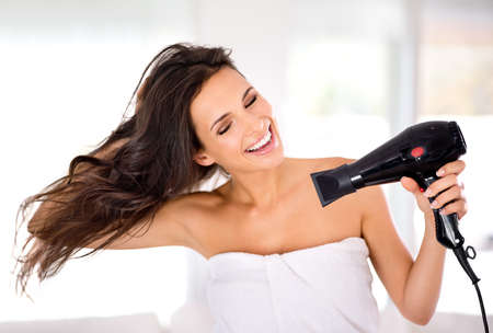 Caring for her hair. A beautiful woman smiling while drying her hair with a hairdryer.の写真素材