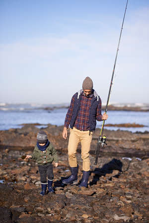 Doing some father and son bonding. Shot of a father and son walking on the rocks while out fishing...