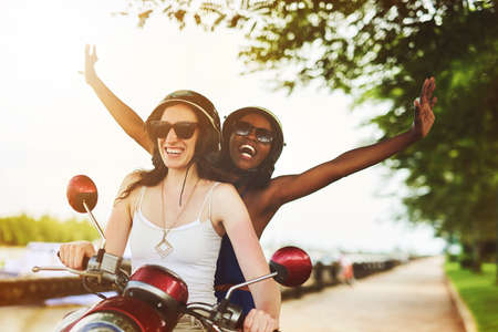 Loving the wind in their hair. Shot of two friends enjoying a ride on a scooter together.の写真素材