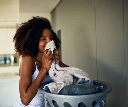 The fragrance of fresh clothing. Cropped shot of an attractive young woman smelling clean laundry at home.の写真素材