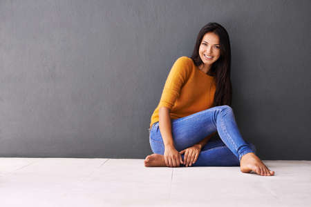 Note to self Relax. Portrait of an attractive young woman sitting against a gray wall.