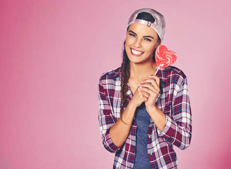 Shes such a sweetheart. Shot of a young woman holding a heart-shaped lollipop against a colorful...