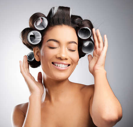 Putting her curls in. Studio shot of an attractive young woman posing with curlers in her hair against a grey background.の写真素材