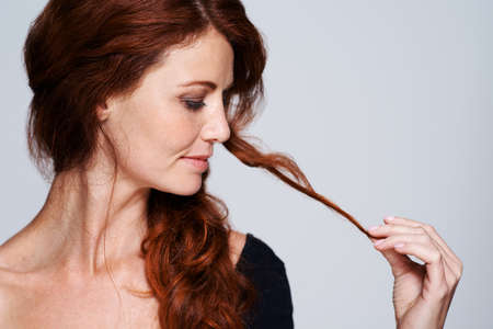 No split ends here. Studio shot of a young woman holding her beautiful red hair against a gray background.の写真素材