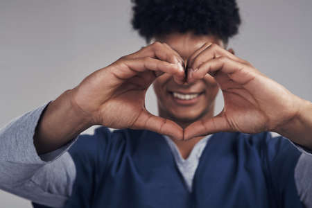We dont just think with our heads, we think with our hearts. Shot of a male nurse forming a heart shape with his hands while standing against a grey background.の写真素材