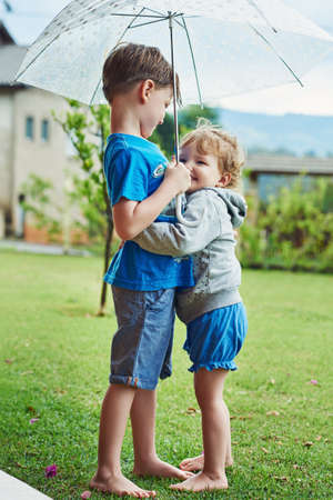 Well stay dry under this umbrella. Shot of a cheerful little boy and girl standing together under an umbrella outside during a rainy day.の写真素材
