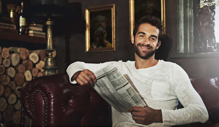 Catching up on current events. Portrait of a handsome man reading a newspaper in a cafe.の写真素材