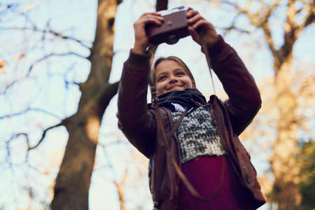 Out on an exploration. Shot of a young girl taking a selfie with a vintage camera outdoors.の写真素材