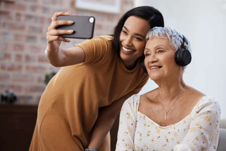 We say I love you with a selfie. Shot of a senior woman using a smartphone to take selfies with her daughter at home.の写真素材