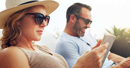Taking a closer look at the menu. Shot of a mature couple sitting side by side on deck chairs and...