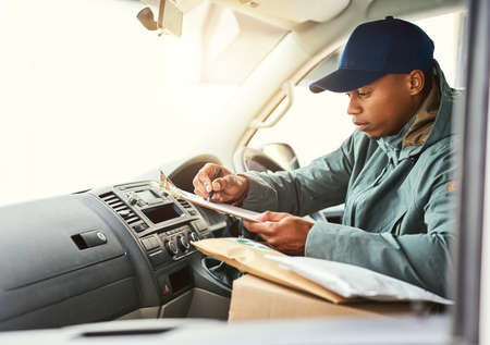 Lets see where to next.... Shot of a courier writing on a clipboard while sitting in a delivery van.