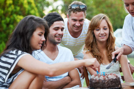 Birthdays are all about sharing. Smiling young teen friends celebrating someones birthday and cutting some birthday cake.の写真素材