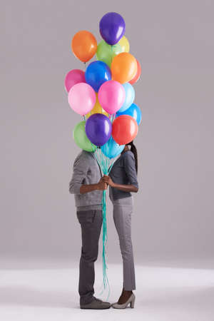 Bonding behind balloons. Studio shot of a couple hiding behind a bunch of balloons.の写真素材
