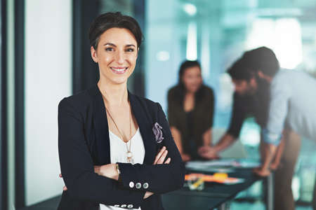 Leading a company that stands by being bold. Portrait of a businesswoman standing in an office with her colleagues in the background.の写真素材