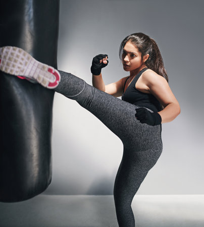 She packs a lot of power in those kicks. Studio shot of a female kickboxer against a gray background.の写真素材