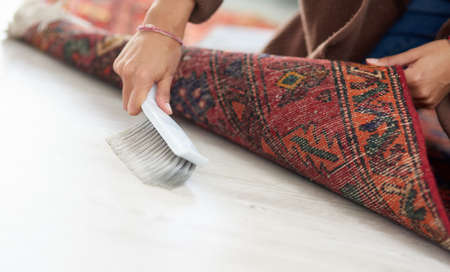 Some people forget this spot but not me. Cropped shot of an unrecognizable woman sweeping under the carpet at home.の写真素材