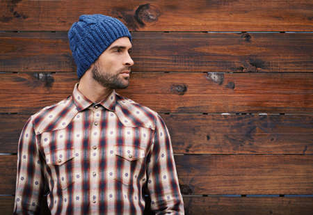 Wear your winter, your way. Shot of a handsome young man in trendy winter attire against a wooden background.の写真素材