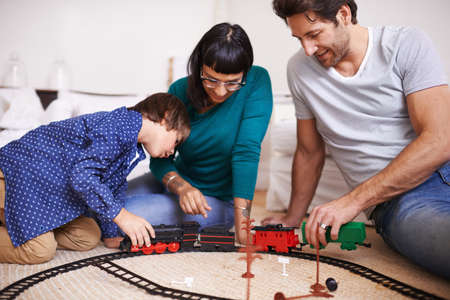 Showing his parents how to hitch the train. Shot of a young family setting up a toy train set.の写真素材