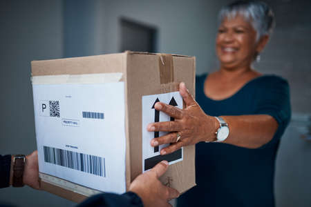 Another package delivered on time, how great. Cropped shot of a package being delivered to a senior woman.の写真素材