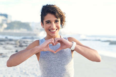 Sharing some summer love. Cropped shot of a woman forming a heart shape with her hands at the beach.の写真素材