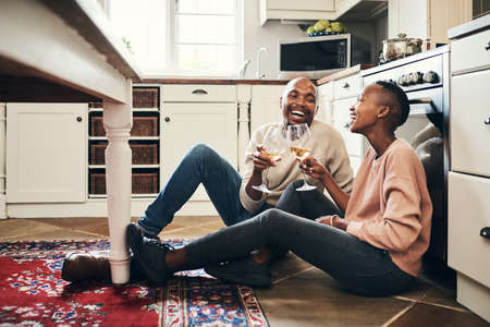 Heres to many more meals together. Full length shot of an affectionate young couple enjoying a glass of wine while preparing dinner in their kitchen.の写真素材
