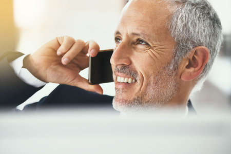 Glad we could connect. Shot of a smiling mature businessman talking on the phone while working in an office.の写真素材