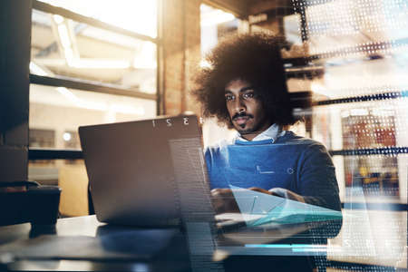 Hes hard at work as always. Shot of a handsome young businessman using a laptop in his office at...