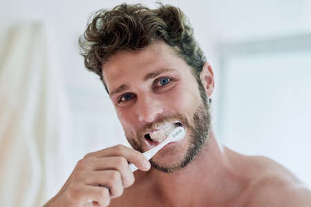 Fresh breath for a great day ahead. Cropped shot of a handsome young man brushing his teeth at home.の写真素材