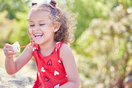 I always get excited about bubbles. Shot of an adorable little girl blowing bubbles at the park.の写真素材