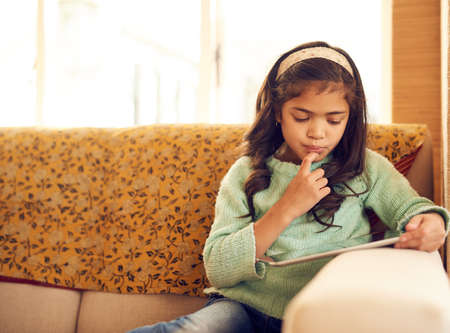 Wireless technology is a great way to encourage independent learning. Shot of a little girl using a digital tablet at home.の写真素材