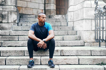 Resting before I take on my next challenge. Full length shot of a handsome young sportsman sitting down on a stairway outdoors in the city.の写真素材