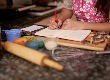 Shes about to bake some tasty treats. Shot of a woman writing in a recipe book.