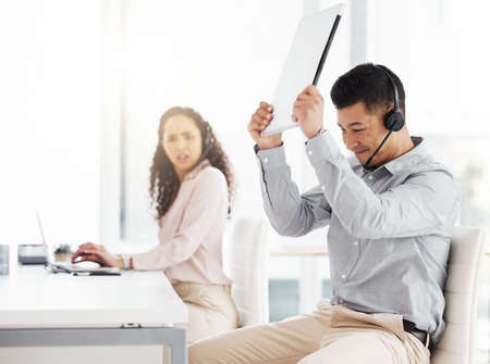 This darn thing wont work. Shot of a young call centre agent angrily smashing a laptop while working...