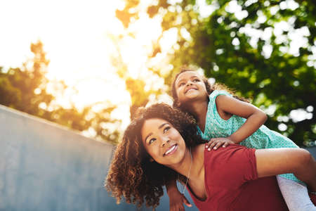 Where to next, little lady. Shot of a happy little girl and her mother enjoying a piggyback ride in their backyard.の写真素材