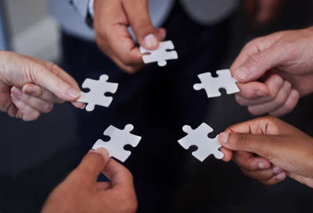 Always welcome help thats offered. Shot of a group of businesspeople putting together puzzle pieces.