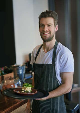 Service with a smile. Cropped portrait of a young waiter taking an order to a customer.の写真素材