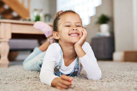 Having fun on her own at home. Portrait of an adorable little girl lying on the floor at home.