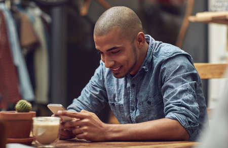Happiness is just a tap away. Shot of a young man using his phone in a cafe.の写真素材