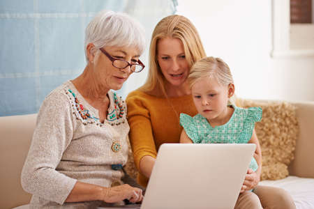 Looking at some family photos in the digital age. Cropped shot of a young woman and her daughter sitting with a laptop indoors.の写真素材