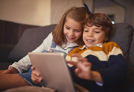 Tech-savvy siblings. Cropped shot of an adorable little boy and his older sister using a digital tablet while sitting on the sofa at home.の写真素材