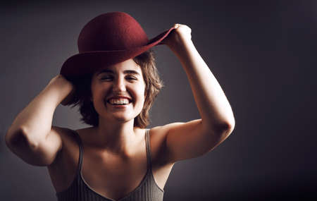 I think it makes me look funny. Stdio shot of an attractive young woman smiling while adjusting her hat against a grey background.の写真素材